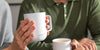 A person holds a White Ember Mug filled with coffee.