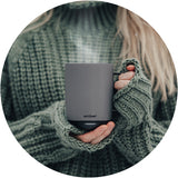 Person in a dark green sweater holding the Ember Mug² in gray with both hands.