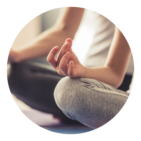 A woman sits with her legs crossed while resting her hands on her knees in a meditative state.