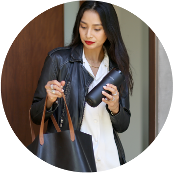 Woman stands outside home looking through bag while holding Ember Travel Mug